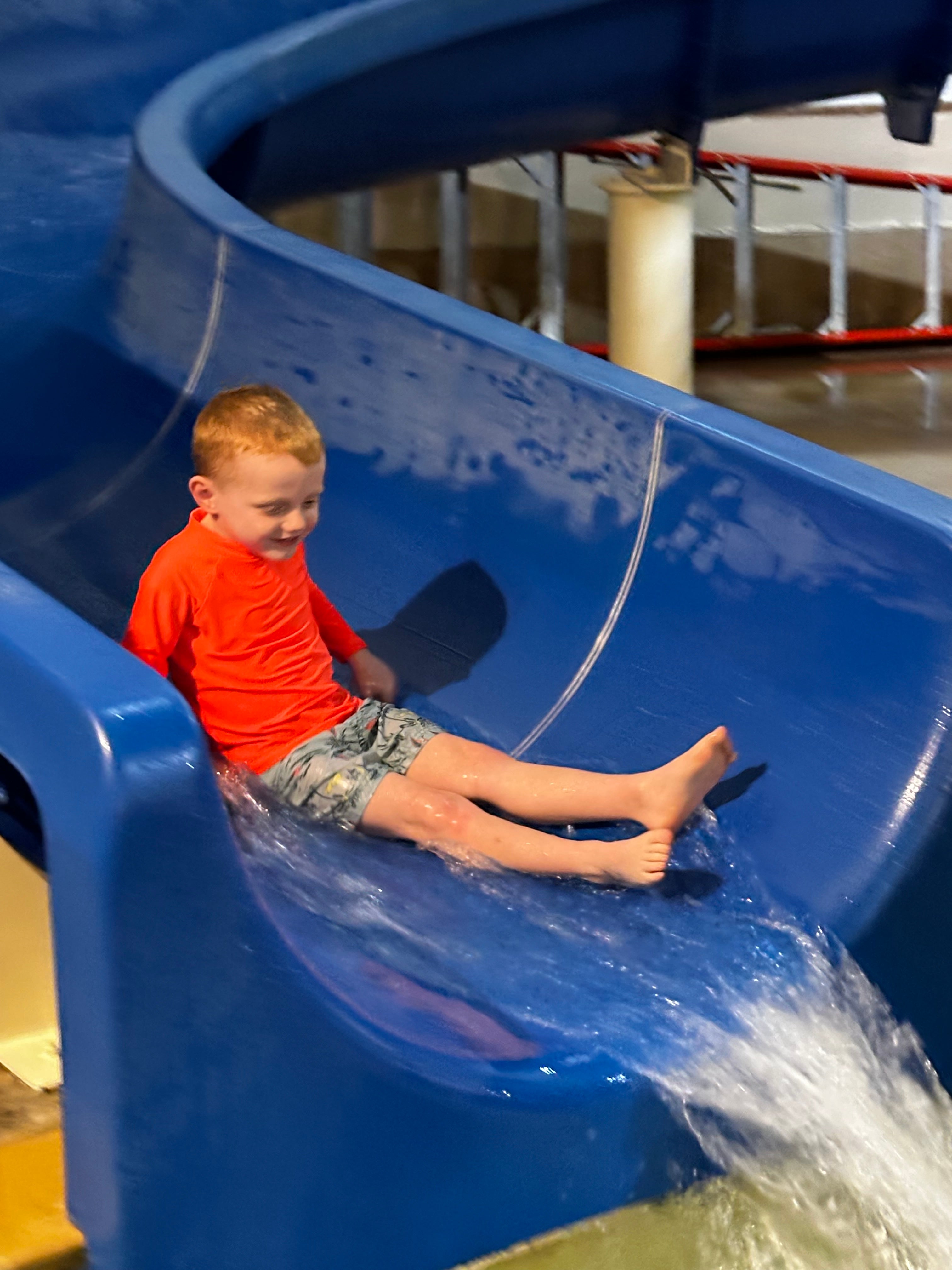 Boy  on the water slide in his neon orange bright rash guard.​