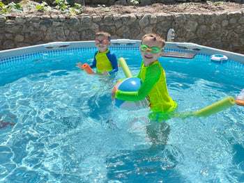 Two boys in a swimming pool standing out from the water color in neon rash guards.