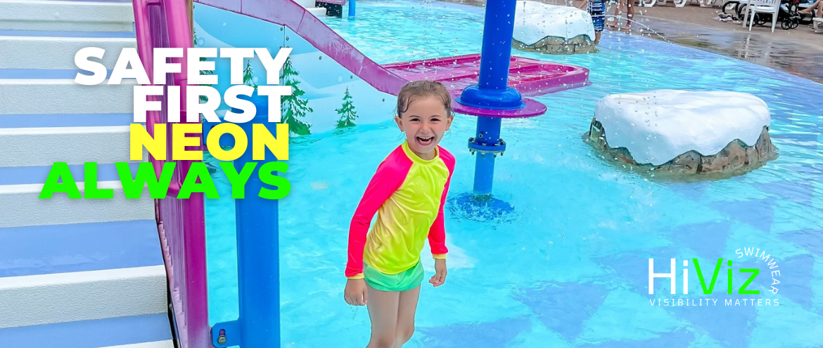 Young girl at the splashed standing in the water smiling. She is wearing her HiViz Neon Rash Guard and stands out from the surroundings.