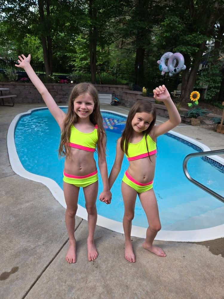 Two girls wearing neon yellow and pink bikinis holding hands by the pool