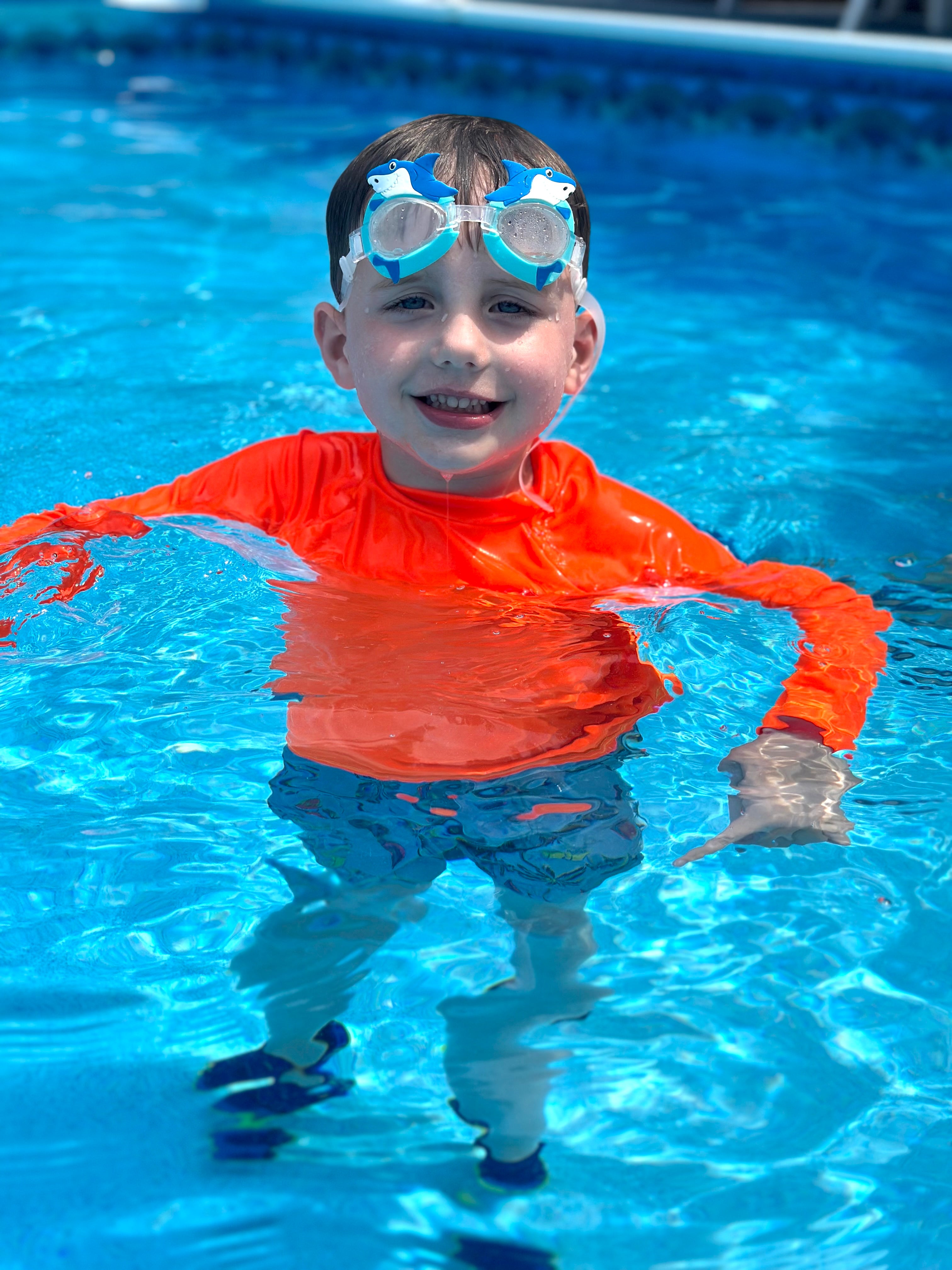 Kids neon swim, neon orange rash guard glowing above and below water. 