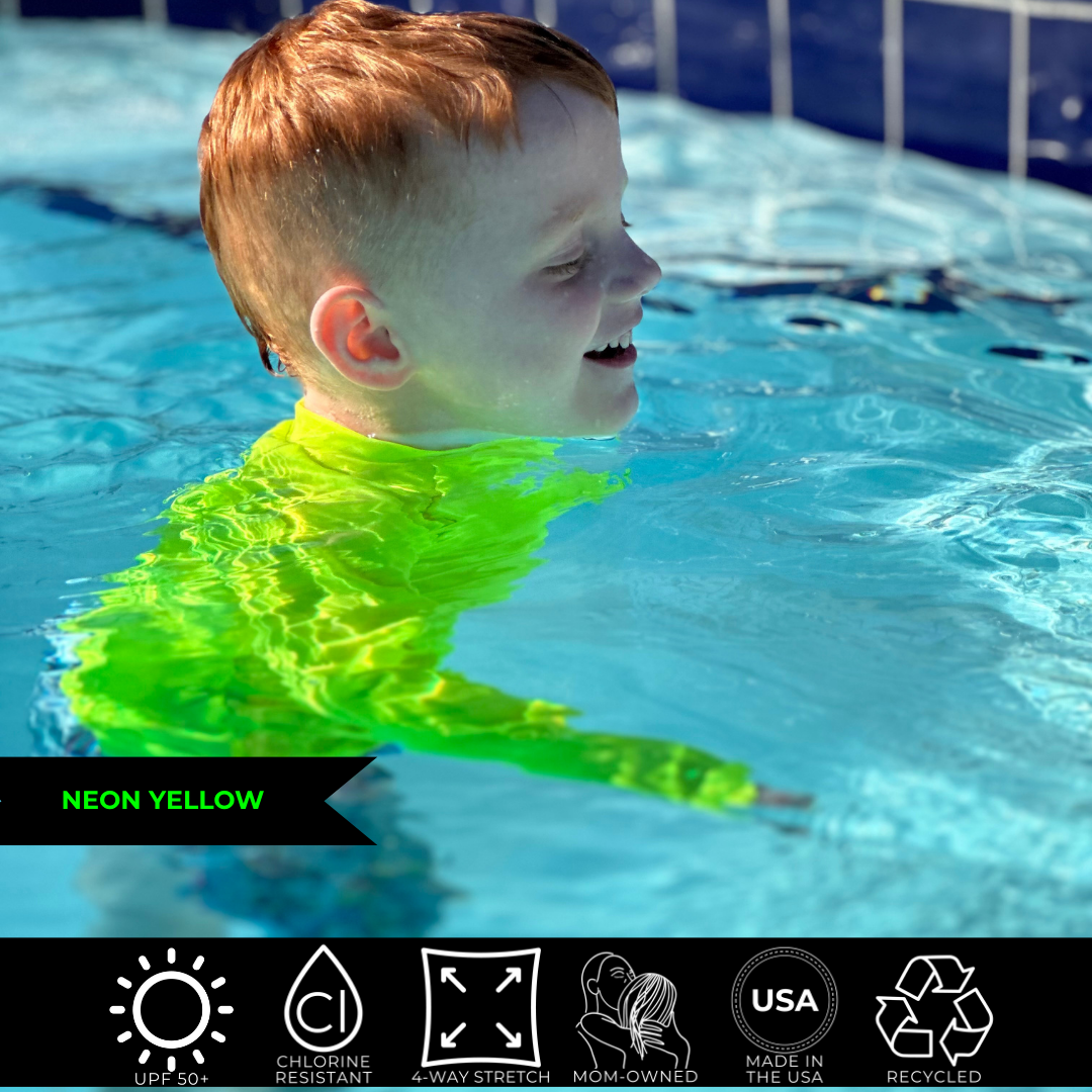 Photo of a boy in a pool wearing a neon yellow rash guard. The rest of him nearly disappears under the water but the neon yellow rash guard is clearly seen. 