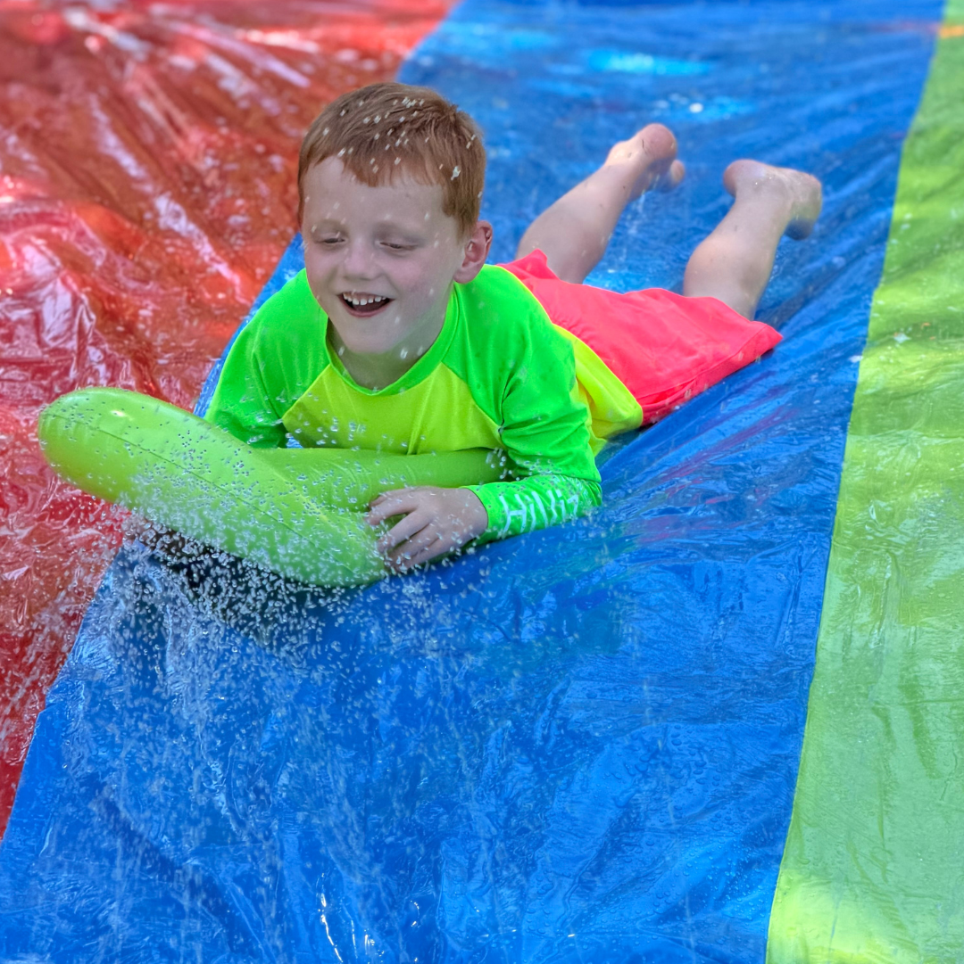 Boy sliding down a waterslide in a neon rash guard and boys neon pink swim trunks hi-viz swimwear for water safety.