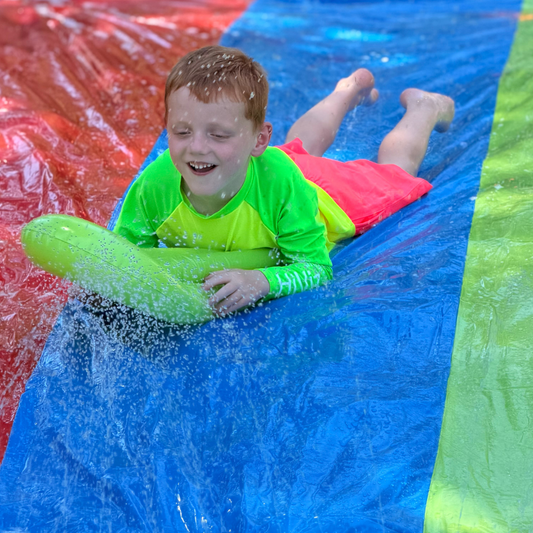 Boy sliding down a waterslide in a neon rash guard and boys neon pink swim trunks hi-viz swimwear for water safety.