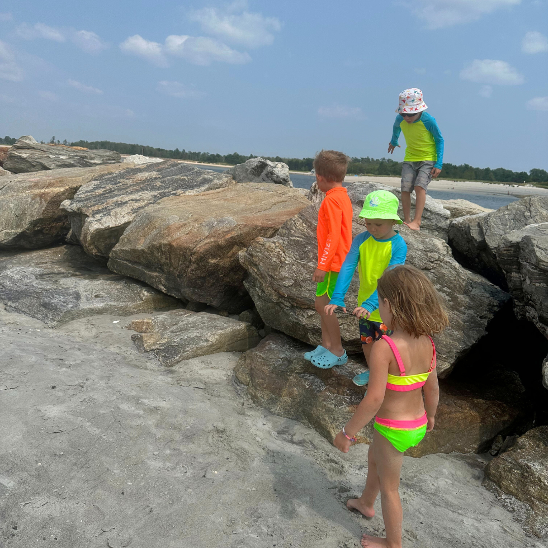 Children in hiviz neon swimwear playing on rocky shoreline with clear sky