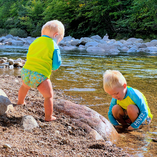 Two children playing by a river with greenery in the background wearing hiviz neon rash guards