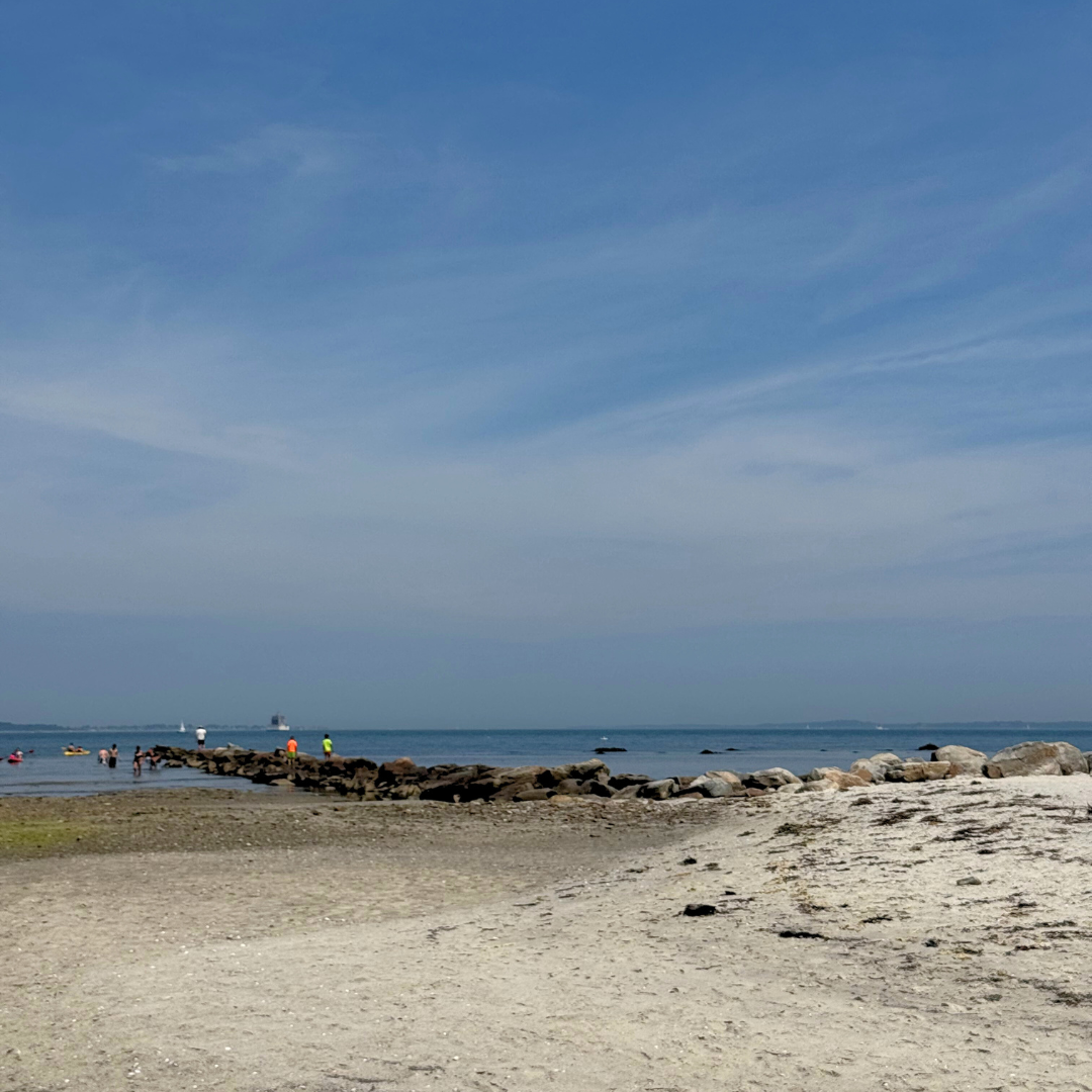 Beach scene with a breakwater and two kids stand out in hiviz neon rash guards there are multiple other people beside the breakwater that blend in.
