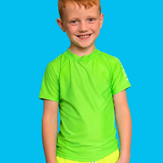 Child standing in front of blue background smiling and wearing a high-visibility neon green rash guard from HiViz Swimwear