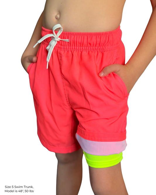 Child wearing hi viz neon pink board shorts with his hands in mesh lined pockets, with neon yellow boxer brief liner showing on the right leg. 