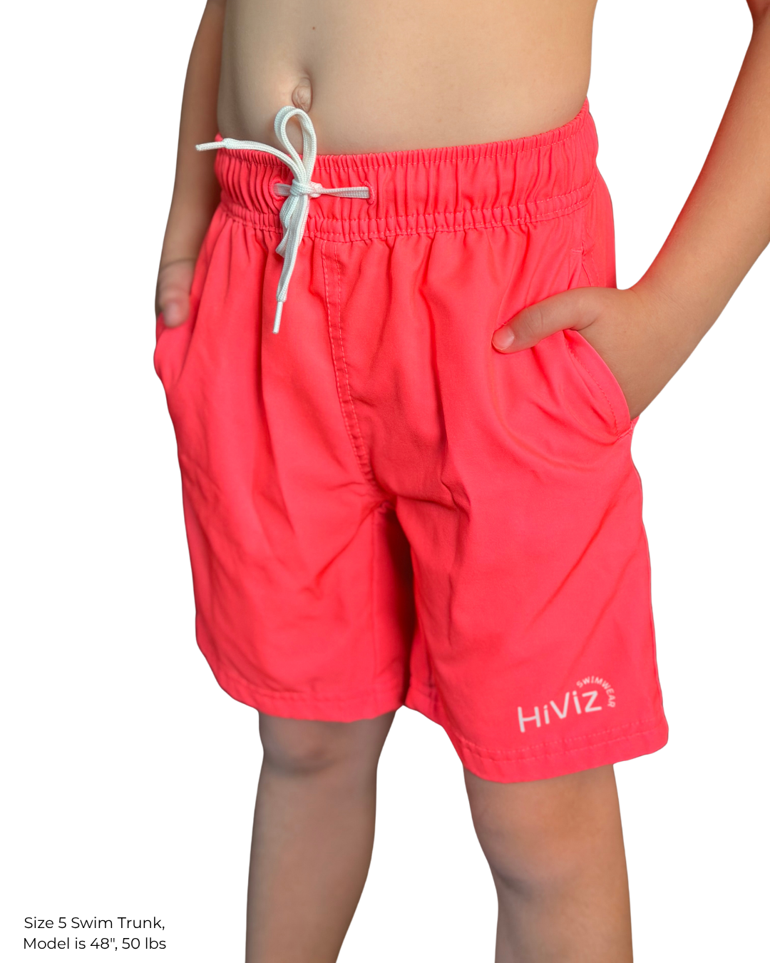 boys standing with his hands in his pockets, wearing hi viz neon pink swim trunks with a white hiviz swimwear logo on the right leg. 