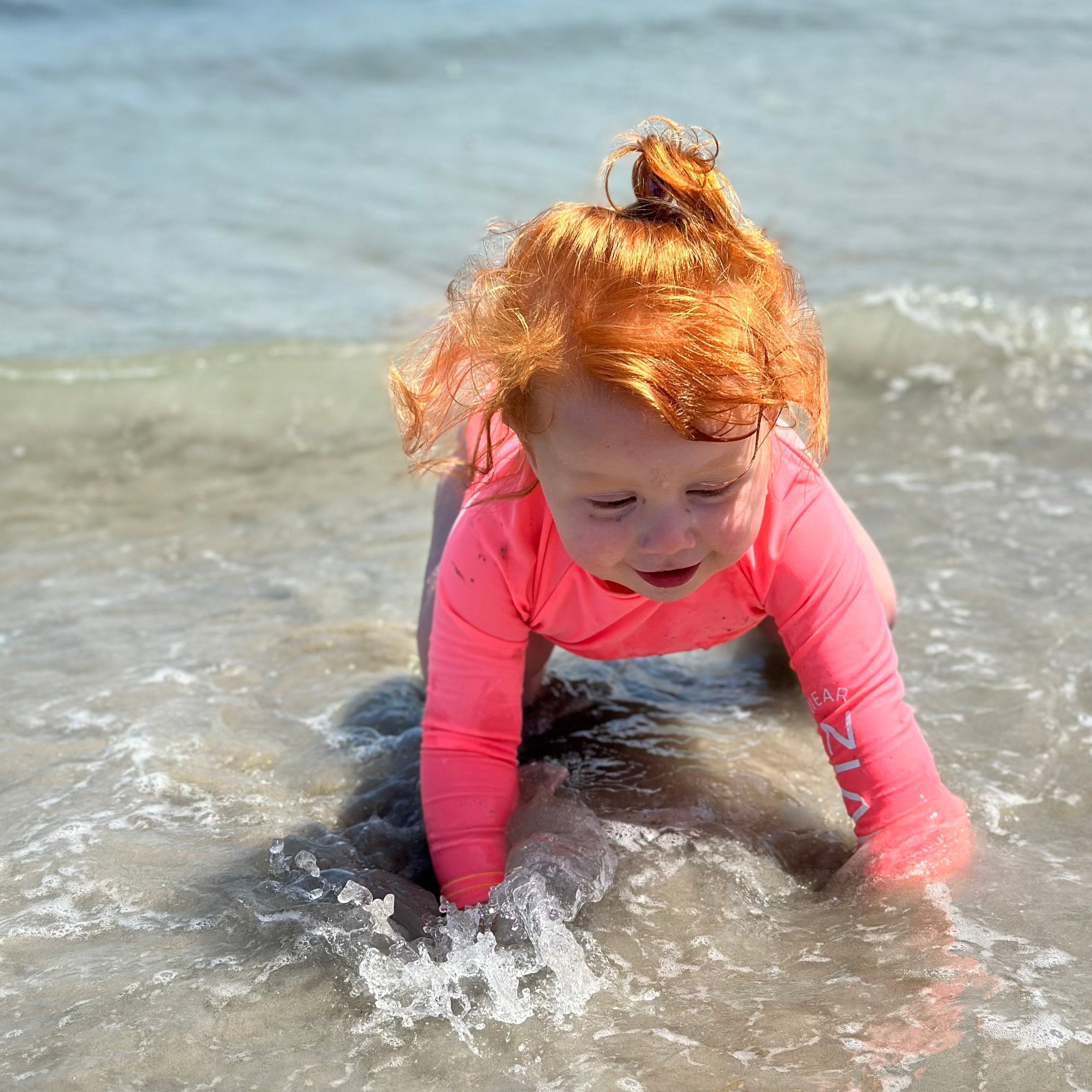 Kids neon swimwear, neon coral toddler rash guard in the ocean.